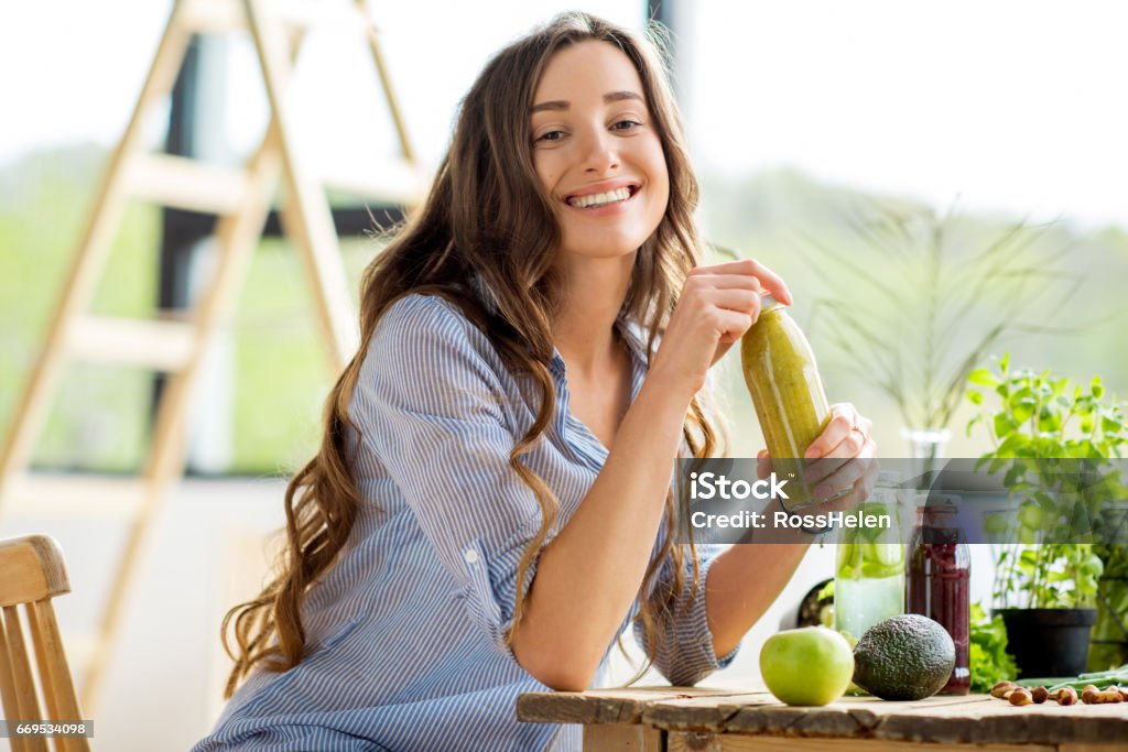 Woman with green healthy food and drinks at home Beautiful happy woman sitting with drinks and healthy green food at home. Vegan meal and detox concept Drinking Stock Photo