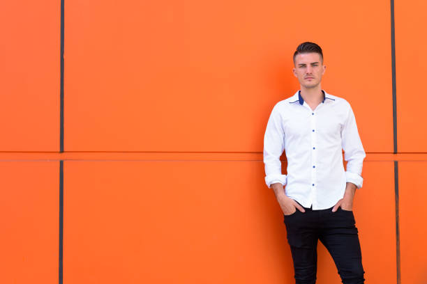 istock Young handsome man standing and leaning against orange concrete wall 669555672