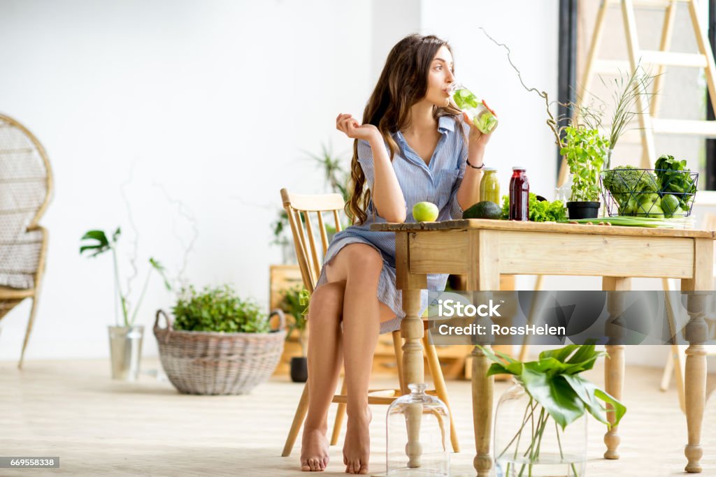 Woman with green healthy food at home Beautiful woman sitting with healthy green food and drinks at home. Vegan meal and detox concept Juice - Drink Stock Photo