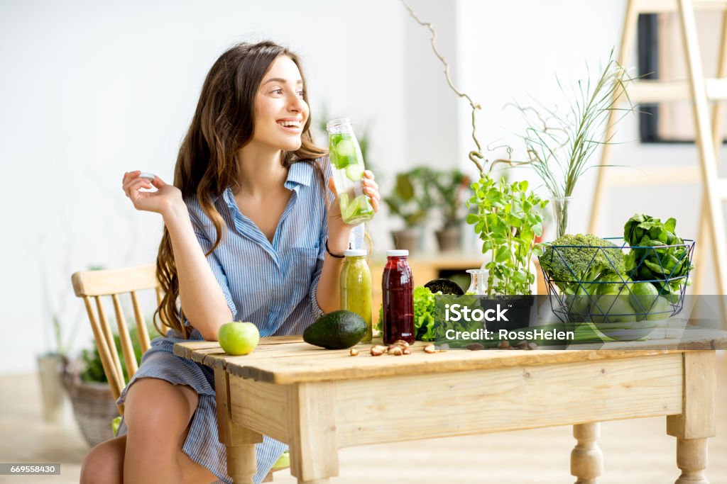 Woman with green healthy food at home Beautiful woman sitting with healthy green food and drinks at home. Vegan meal and detox concept Detox Stock Photo