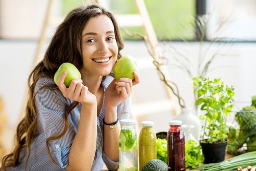 Portrait of a beautiful woman sitting with apples at home. Vegan meal and detox concept