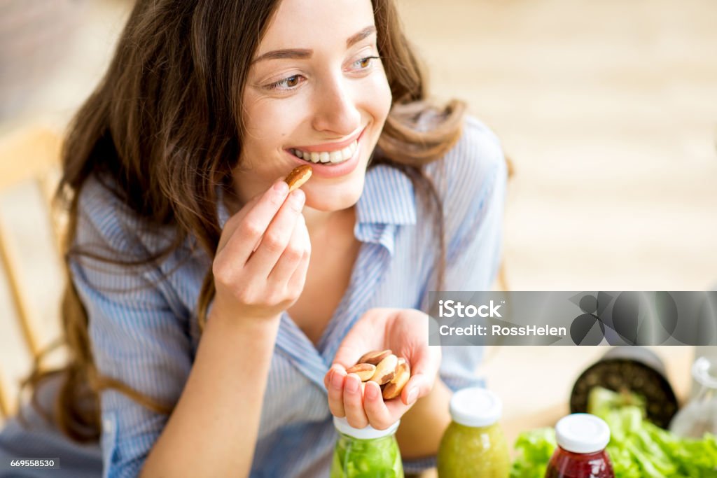 Woman eating nuts Closeup view from above of a woman eating brasil nuts with healthy food on the background Nut - Food Stock Photo