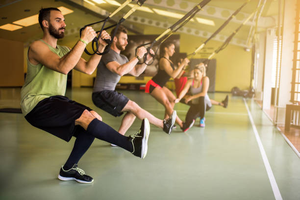 Group of athletes doing strength exercises on suspension training in a health club. Young athletic people having a cross training in a health club. suspension training stock pictures, royalty-free photos & images