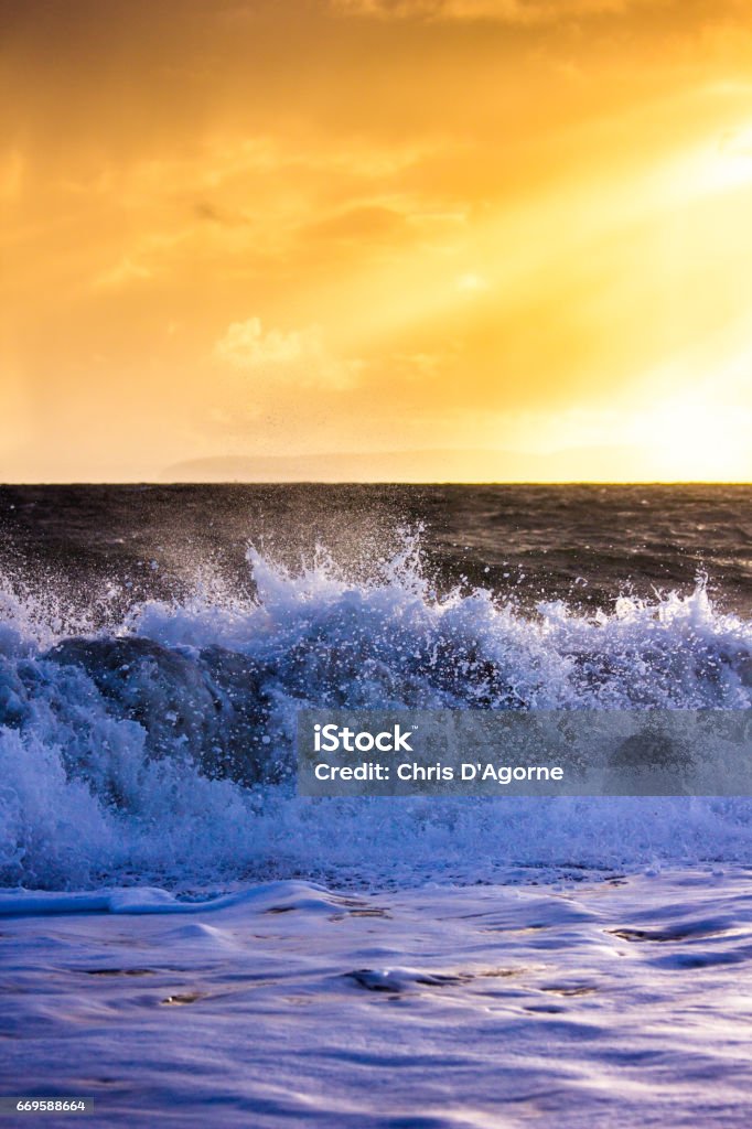 Waves Crash Onto the Beach at Hengistbury Head in a Dramatic Winter Storm Waves break over the shingle beach at Hengistbury Head, Dorset with the Isle of Purbeck visible in the distance against the sun. Beach Stock Photo