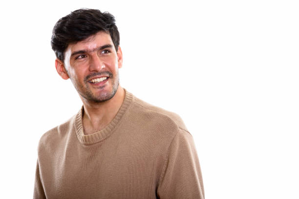 Studio shot of young happy Persian man smiling while thinking and looking up horizontal shot