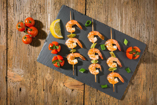 istock Shrimp skewers with tomatoes and herbs and lemon on a stone 669603624