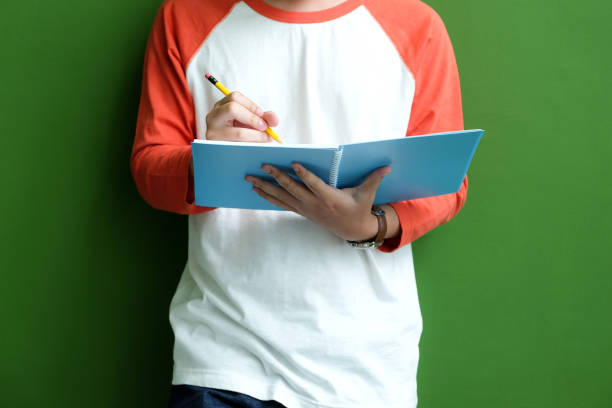 istock Young man writing on notebook paper while standing in front of  green wall background, education background 669610530