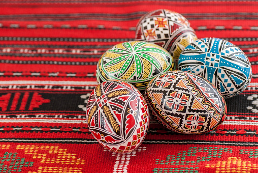 Two colorful hand painted pink and multi coloured green blue and yellow ornate Easter eggs on bright off white cream colored background against a wooden brown rustic woven wicker basket for of Easter holidays celebration with copyspace. Apt for use as greeting cards, posters wallpaper and backdrops.