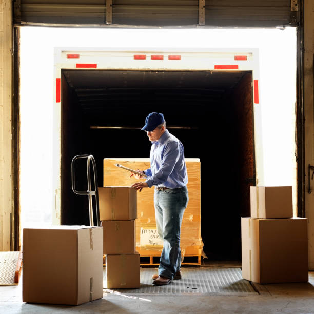 Warehouse Shipment Worker standing at the rear of a delivery truck while reviewing a warehouse shipment. loading bay stock pictures, royalty-free photos & images