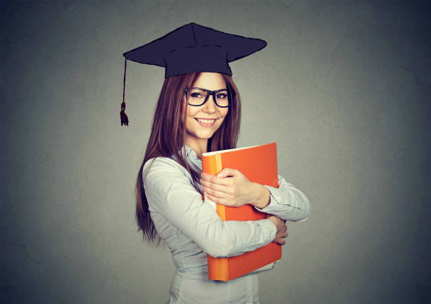 istock Graduate student woman in cap gown with folder looking at camera 669653080