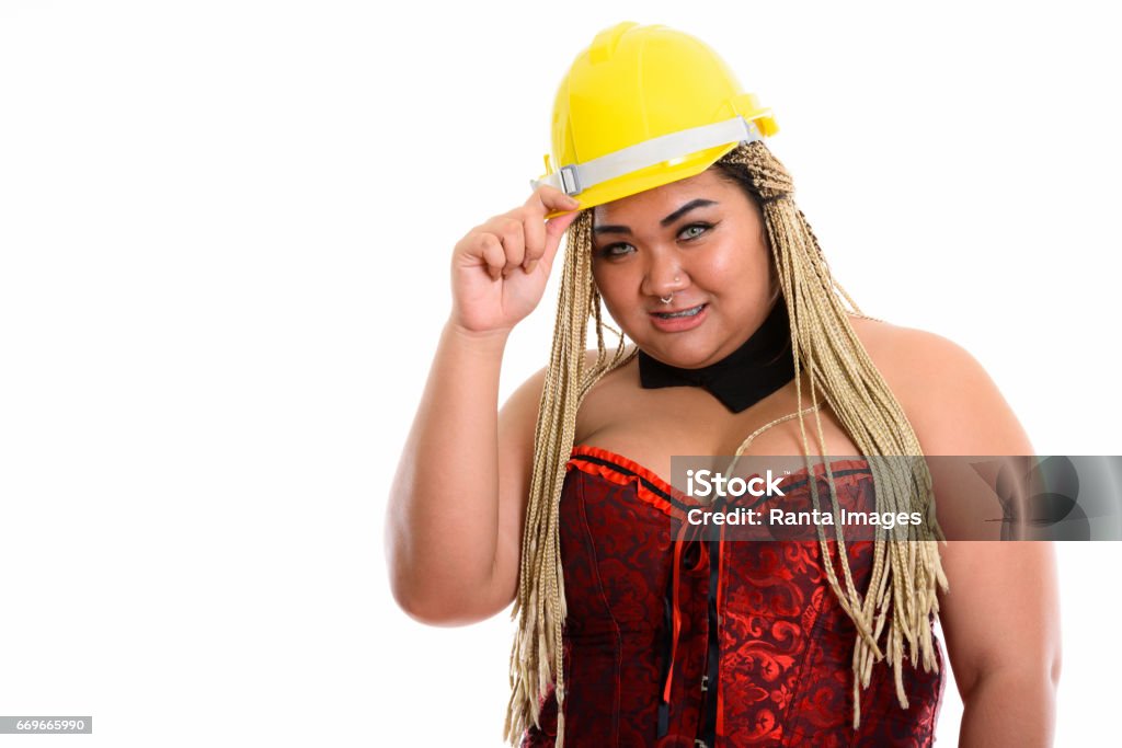 Young happy overweight Asian construction woman smiling while holding safety helmet and wearing sexy costume Young happy overweight Asian construction woman smiling while holding safety helmet and wearing sexy costume horizontal shot Dental Braces Stock Photo