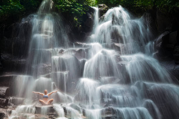 istock Woman sit on rock in yoga pose under cascade waterfall 669670524