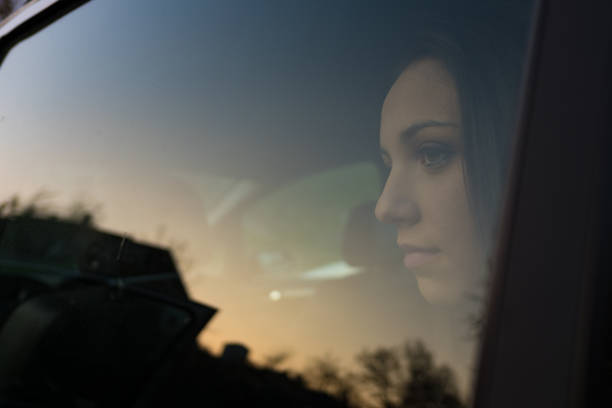 Young serene woman sitting in the backseat of a car and looking away, trees reflecting on the car window glass, travel concept