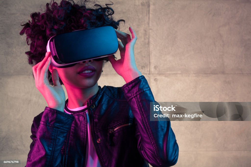 Young girl with VR goggles on head Pretty young African girl adjusting the VR headset on the white background Virtual Reality Simulator Stock Photo