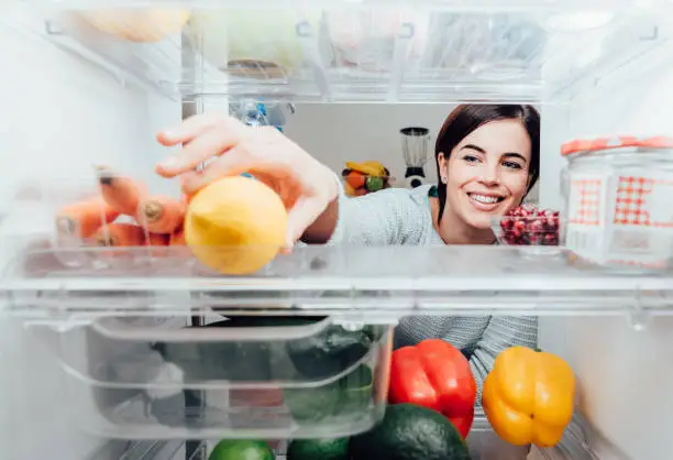 Smiling woman taking a fresh lemon out of the fridge, healthy food concept