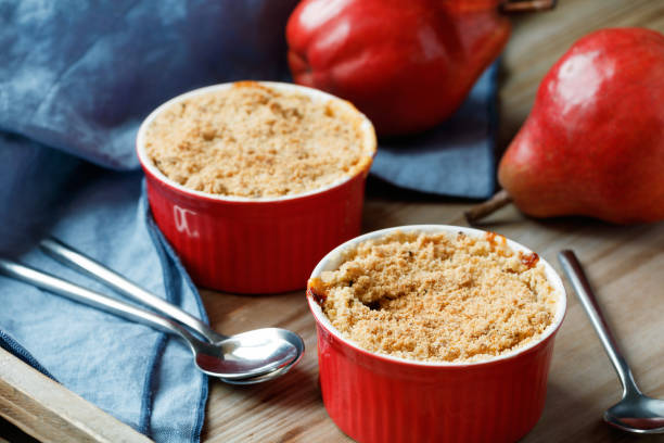 plan rapproché d’une tarte de crumble de poire de portion de dessert dans un bol rouge sur une table en bois. - pie fruit cobbler sweet food photos et images de collection