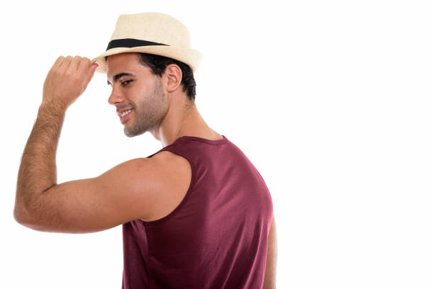Profile view of young happy Hispanic tourist man smiling while looking back and holding hat horizontal shot