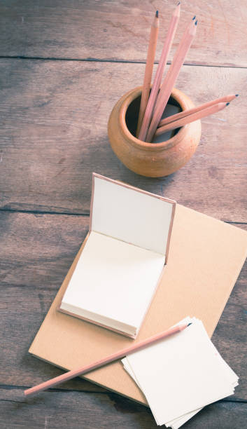 istock Blank notebook with pencils in clay pot on wooden table, split toning effect 669712408