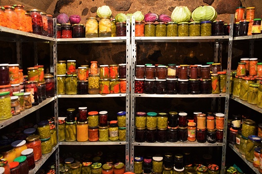 Basement larder with all the home canned goods. We see the fruits and vegetables in the jars on the metal shelves.