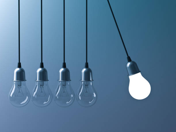 istock One hanging light bulb glowing different and stand out from unlit incandescent bulbs like newtons cradle on dark cyan background, leadership and different business creative idea concept. 3D rendering 669719658