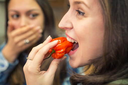 Girl biting habanero chilli pepper. Young woman tasting chilli pepper.