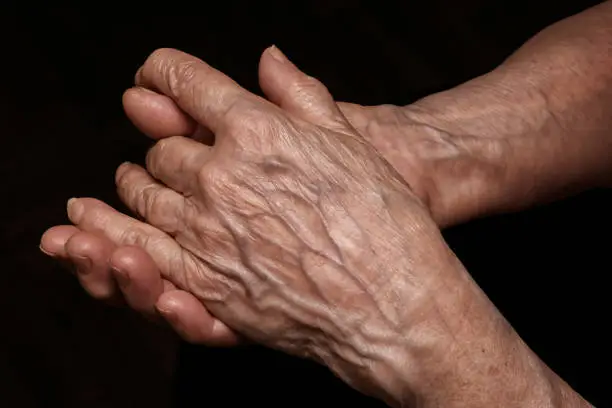 Folded senior woman wrinkled hands close up. On abstract background, clipping path included. Old age, age problems, poverty and loneliness theme