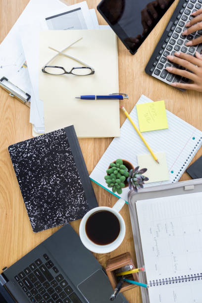 Unrecognizable businesswoman works from home. She using a digital tablet with a keyboard. A laptop, coffee cup, personal organizer and other items are on the desk.