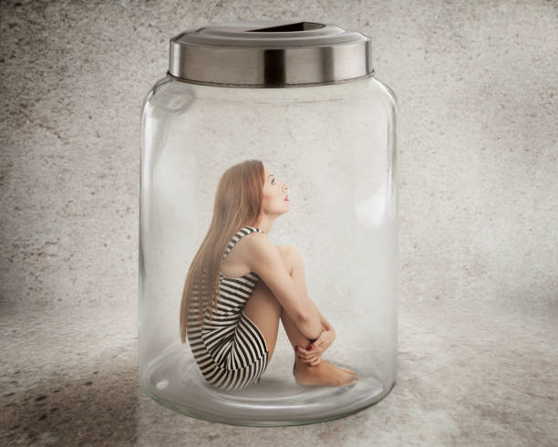 Young lonely woman sitting in glass jar Lack, violation of human rights liberty. Young lonely woman sitting in glass jar isolated grey wall background. Suppression of freedom, restrain, employee working conditions, life limitation concept trapped stock pictures, royalty-free photos & images