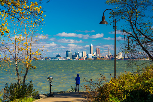 A woman wearing a hood looks at the Cleveland Skyline from a park just beside Lake Erie\