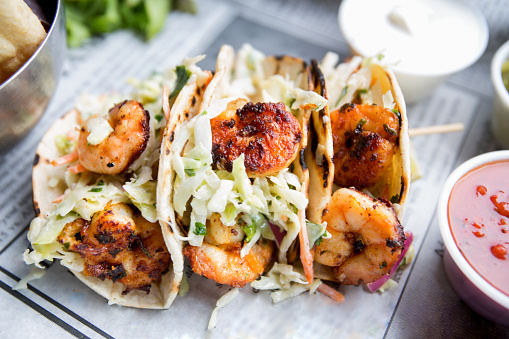 Grilled jumbo shrimp in corn tortilla tacos with cabbage garnish on an old fashioned newspaper wrapper.