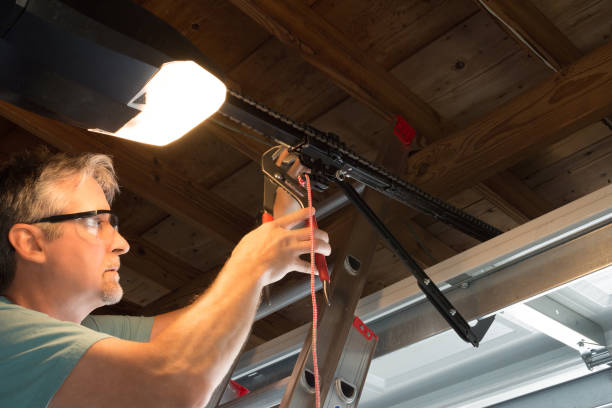 Professional automatic garage door opener repair service technician working closeup Closeup of a professional automatic garage door opener repair service technician man working on a ladder at a home residential location making adjustments and fixing it while installing it. door repairman men manual worker stock pictures, royalty-free photos & images