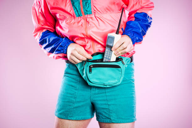 Nineties Tech and Fashion Style Man A man wearing fluorescent colored clothing puts a 1980's - 1990's cellular brick phone into his fanny pack, representing state of the art style and technology for that time.  Detail shot; horizontal with pink background. garment photos stock pictures, royalty-free photos & images