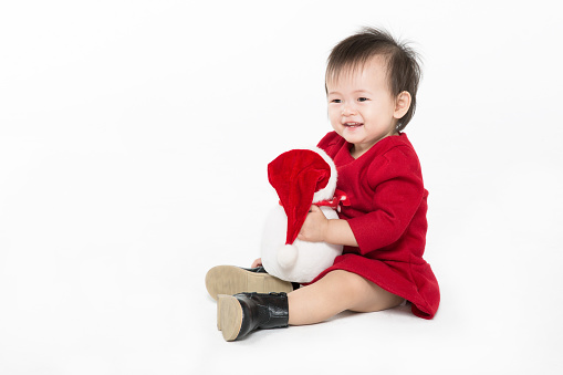 Christmas toddler girl sitting and taking snowman toy in her arms on white background.