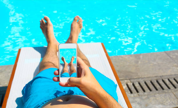 Young man lying on sunbed near pool with phone Young man lying on sunbed near pool with phone. Summer vacation and travel concept male foot model stock pictures, royalty-free photos & images