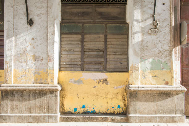 This is a horizontal, color photograph of a distressed, exterior wall with closed windows in Havana, Cuba.