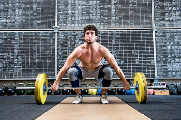 Bodybuilder preparing to lift barbell Bare chested male bodybuilder preparing to lift heavy barbell in gym clean and jerk stock pictures, royalty-free photos & images