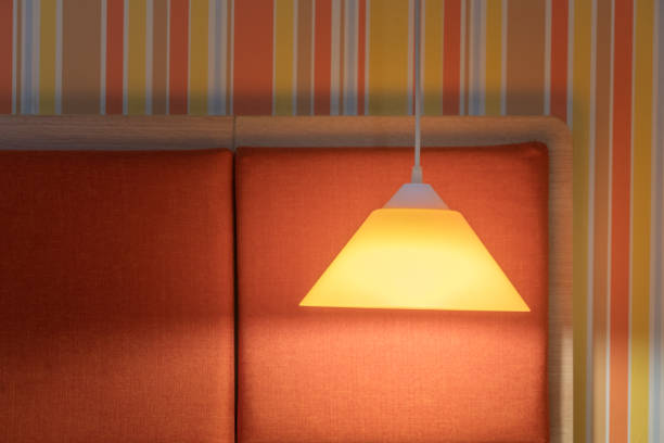 Lamp and shade colourfuly lit with a patterned wallpaper background