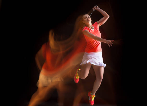 istock Young woman playing badminton over black background 669876256