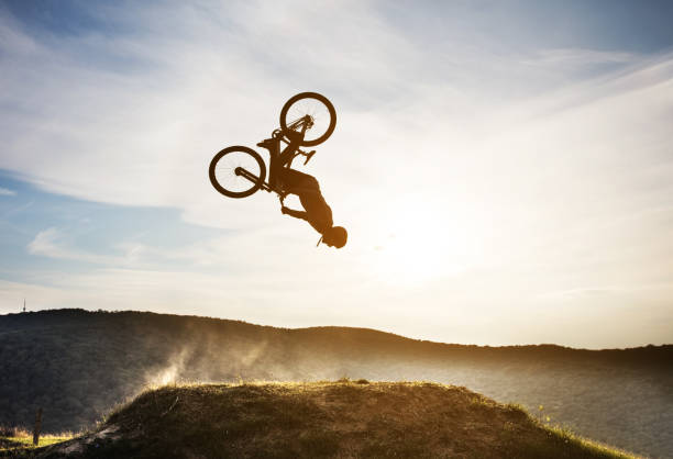 Man on mountain bicycle performing backflip in nature. Skillful mountain bike cyclist practiocing in nature and practicing backflip against the sky. bicycle stunts stock pictures, royalty-free photos & images