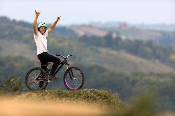 Mountain bike cyclist with arms raised on top of hill. Young smiling man on mountain bicycle looking at camera with his hands raised. x games stock pictures, royalty-free photos & images