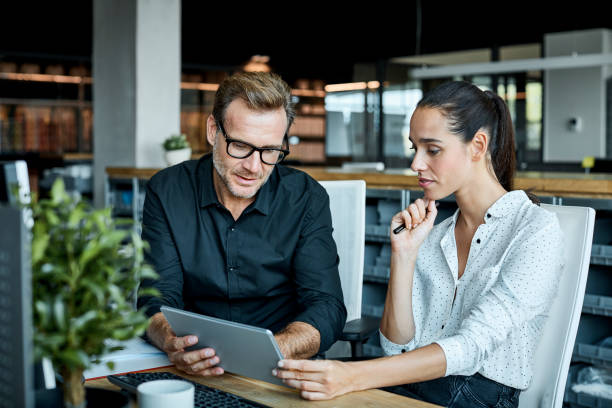 Colleagues using tablet PC in textile factory Male and female colleagues looking at tablet PC. Business people are working at desk. They are sitting in textile factory. business casual stock pictures, royalty-free photos & images