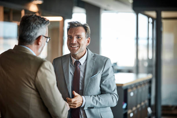 Businessmen communicating in textile factory Senior businessman smiling while looking at colleague in textile factory. Professional is wearing suit while looking at coworker. They are communicating in office. synergy series stock pictures, royalty-free photos & images