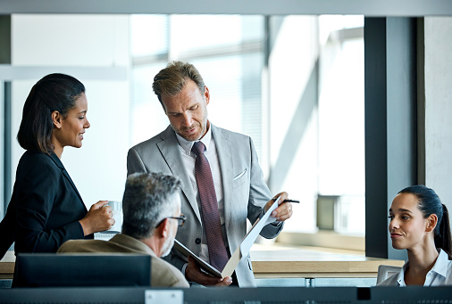 Confident businessman reading documents while standing by colleagues. Male and female professionals are in textile factory. Executives are working in office.