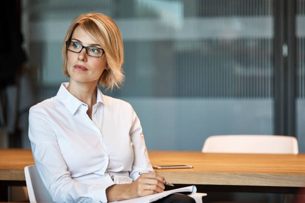 Thoughtful businesswoman looking away at desk Thoughtful businesswoman looking away at desk. Female executive is writing in textile factory. Professional is with short blond hair. senior management stock pictures, royalty-free photos & images