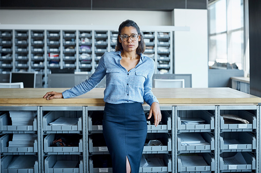 Portrait of confident businesswoman leaning on counter. Young executive is standing in textile factory. She is wearing smart casuals.