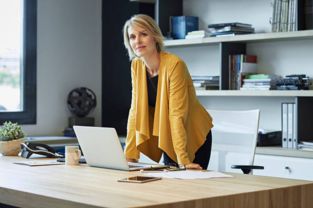 confident businesswoman leaning on desk - 30s women sweater female foto e immagini stock