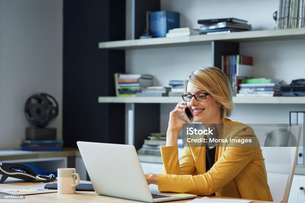 Mujer de negocios con ordenador portátil y teléfono inteligente en el escritorio - Foto de stock de Usar el teléfono libre de derechos