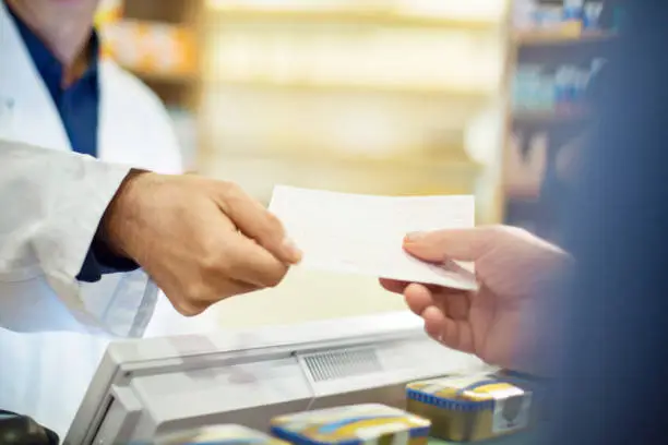Cropped image of senior man taking bill from male pharmacist in store. Chemist is selling medicines to customer at pharmacy. He is wearing lab coat.