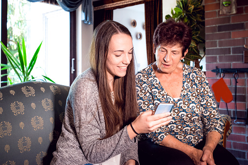 Grandmother and her granddaughter learning how to Text Message and use a smart phone in the living room