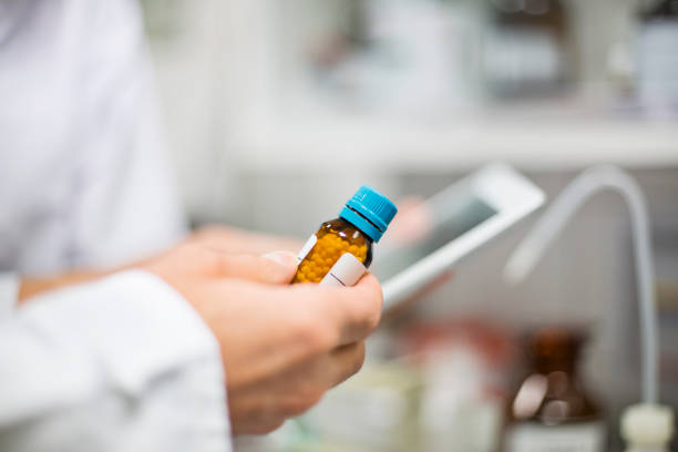 scientist holding pill bottle and digital tablet - homeopatic medicine imagens e fotografias de stock